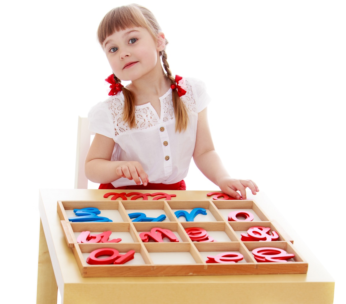 A child at a table with a wooden tray of the Montessori Movable Alphabet, its colored letters sorted into compartments
