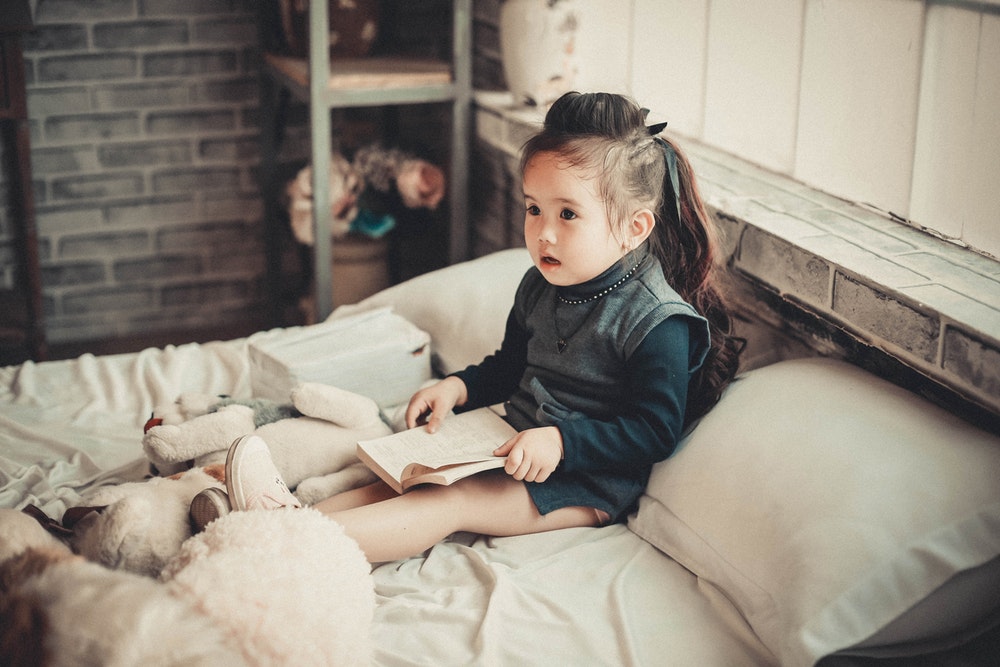 A young child sitting quietly with an open book, reading on her own