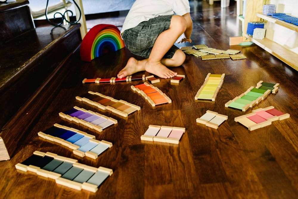 An adult calmly demonstrating a Montessori activity to a young child at a low table