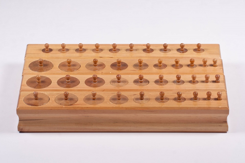 A child carefully placing a wooden cylinder into its matching socket in a Montessori classroom