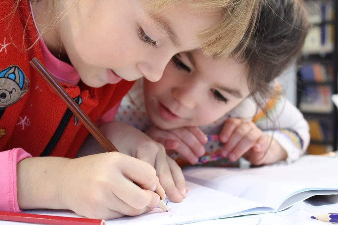 Two young children drawing together with colored pencils in a notebook
