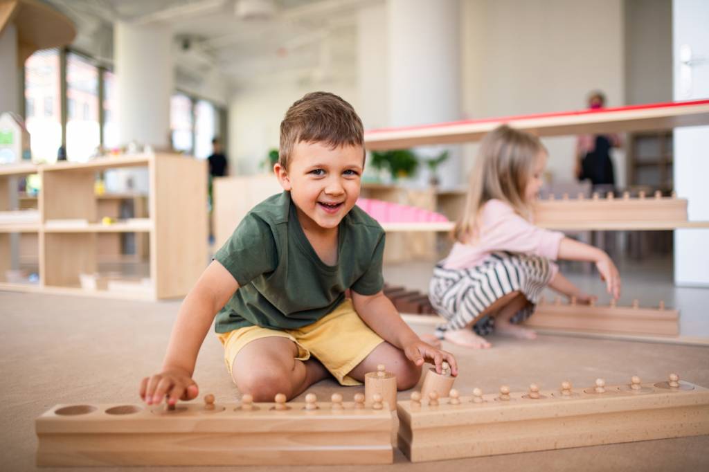 A smiling boy working with the Montessori knobbed cylinder blocks on the floor of a prepared classroom