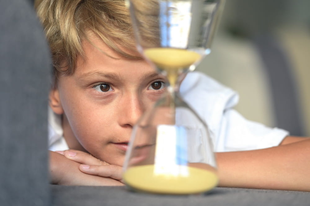 A child looking through an hourglass, illustrating the Montessori timeline materials' focus on the passage of time