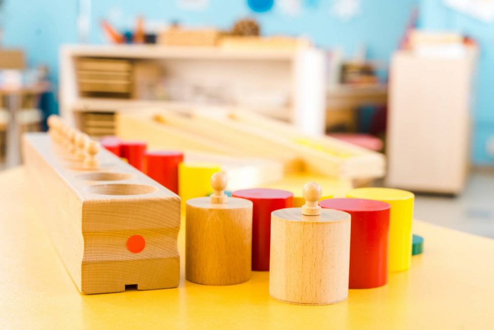 Wooden Montessori materials, including the Cylinder Blocks, arranged on a table in a classroom