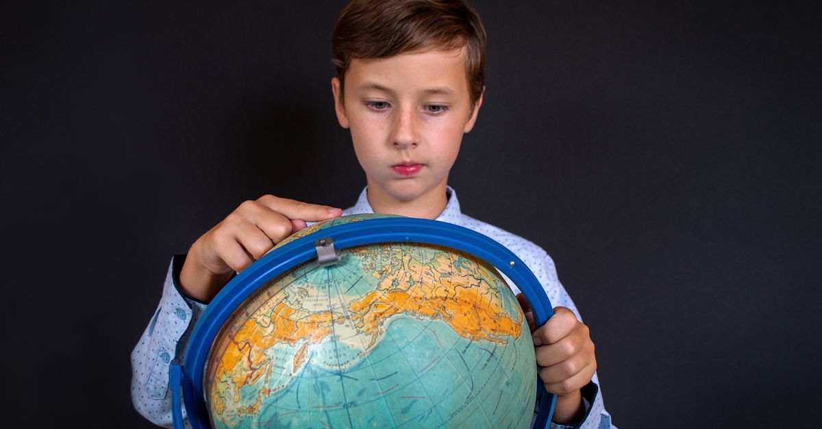 A boy studying a world globe, tracing the continents and oceans with his hands