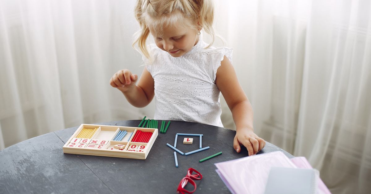 A young child at a table with a wooden number box and colored counting rods, arranging the rods to count