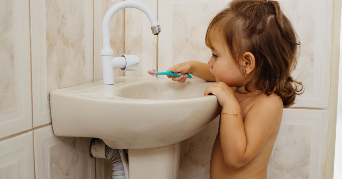 A toddler standing at a bathroom sink brushing their teeth, practicing an everyday self-care task