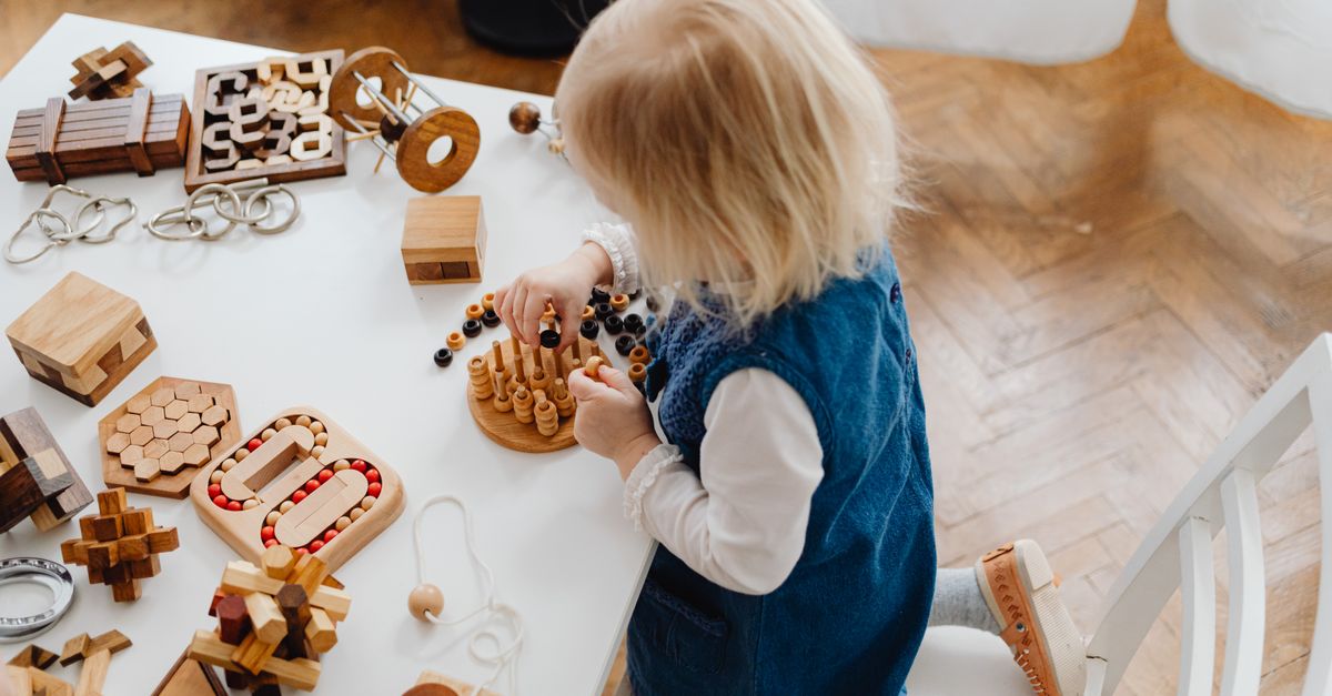 A toddler at a table exploring an assortment of wooden sensory blocks and manipulatives with her hands