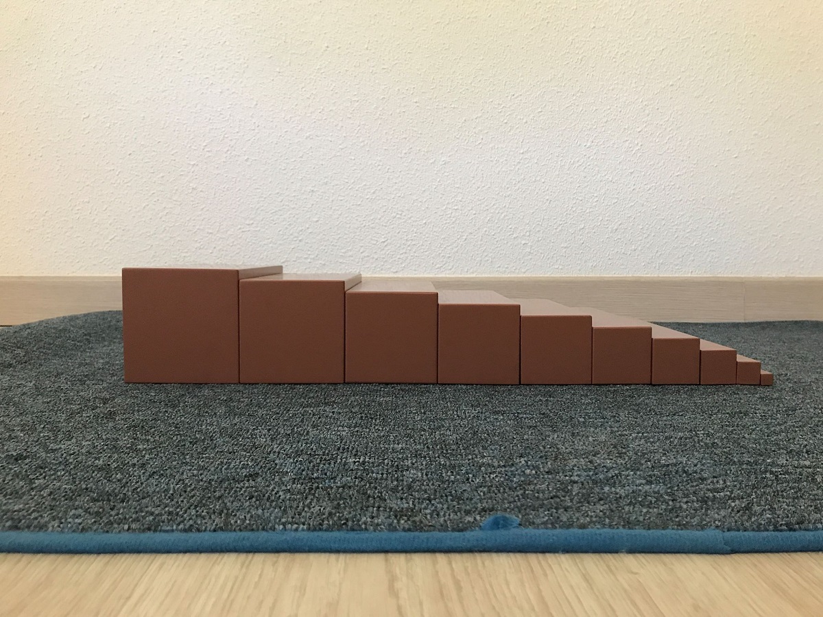 The Montessori Brown Stair arranged as a descending staircase of ten dark brown prisms on a floor mat