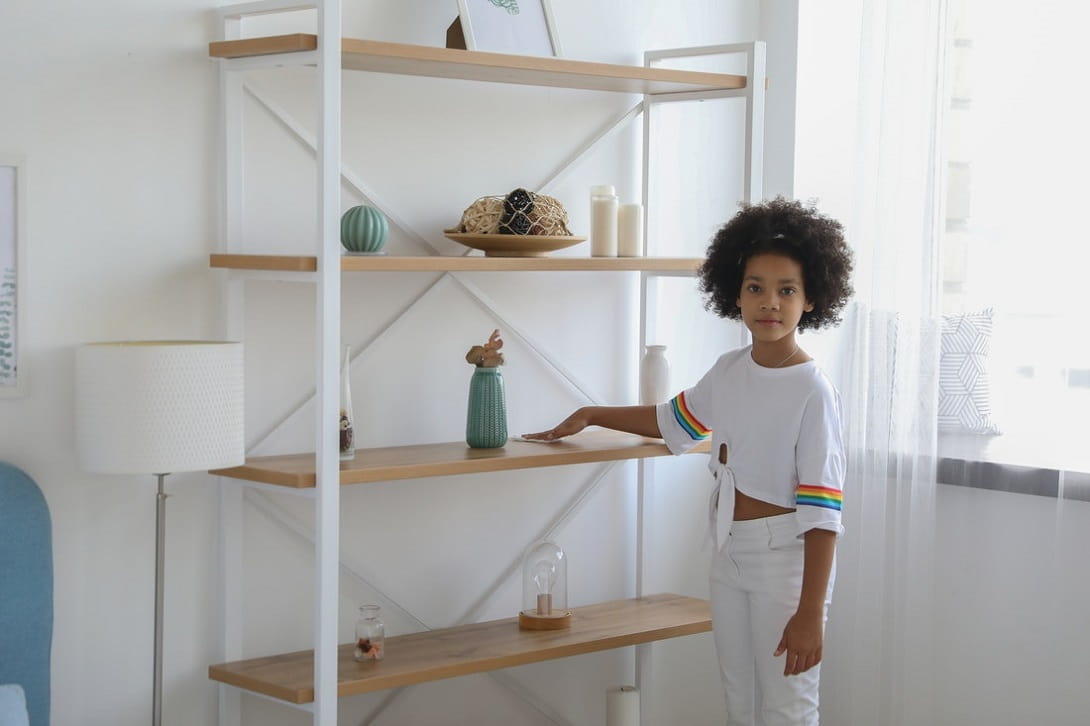 A young child tidying and arranging objects on an open shelf at home
